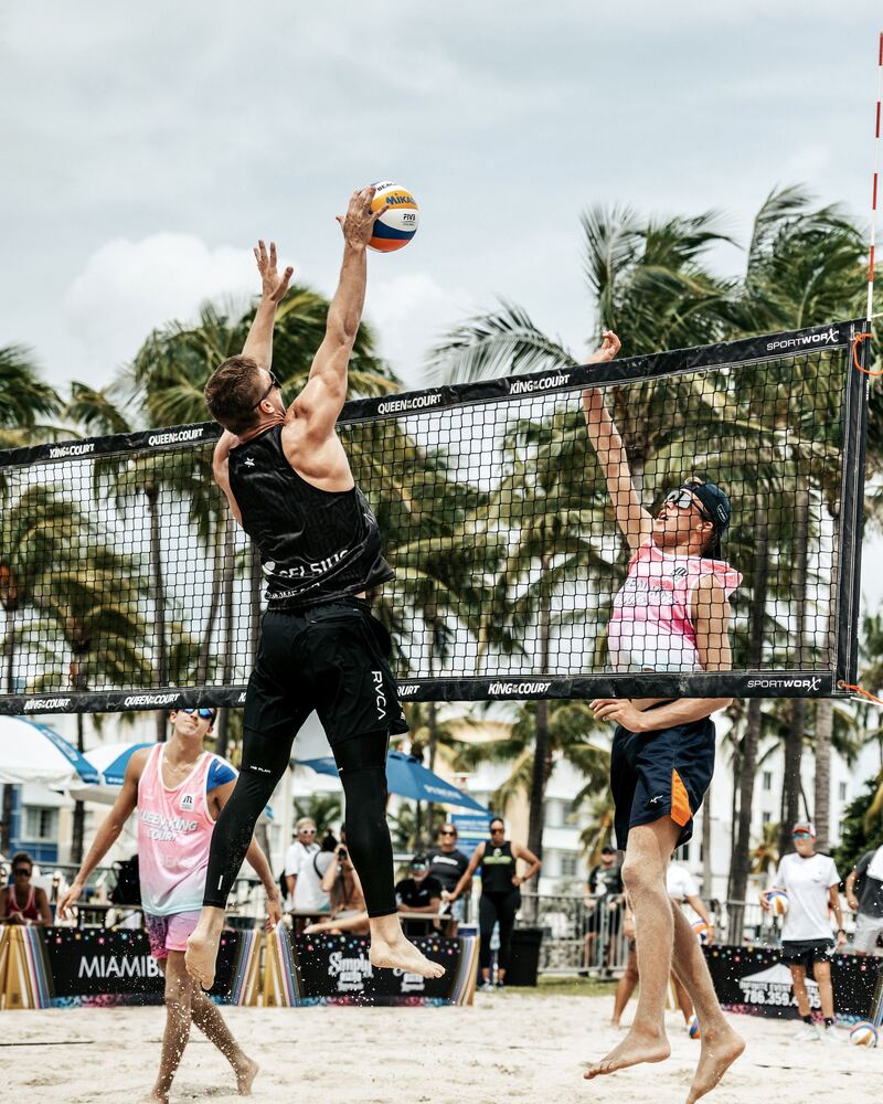 Aidan Patterson elevating for a block at the net in a beach volleyball tournament